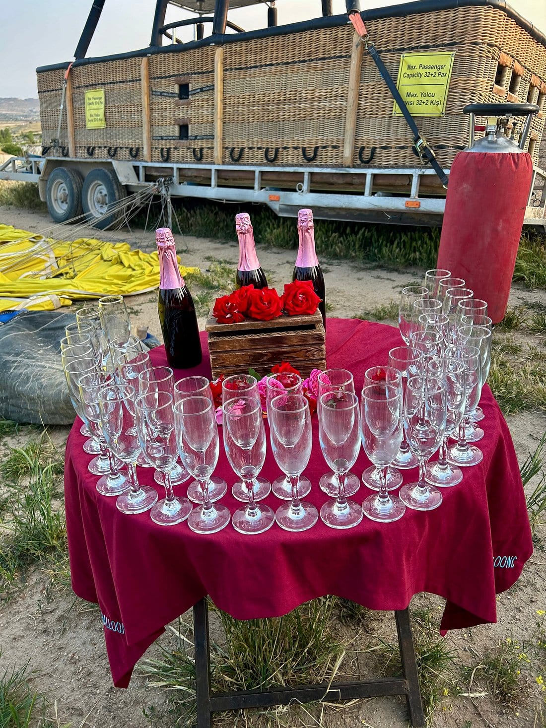 Un tavolo apparecchiato con spumante rosé, rose e file di calici per la cerimonia dopo il volo accanto al rimorchio della cesta in Cappadocia
