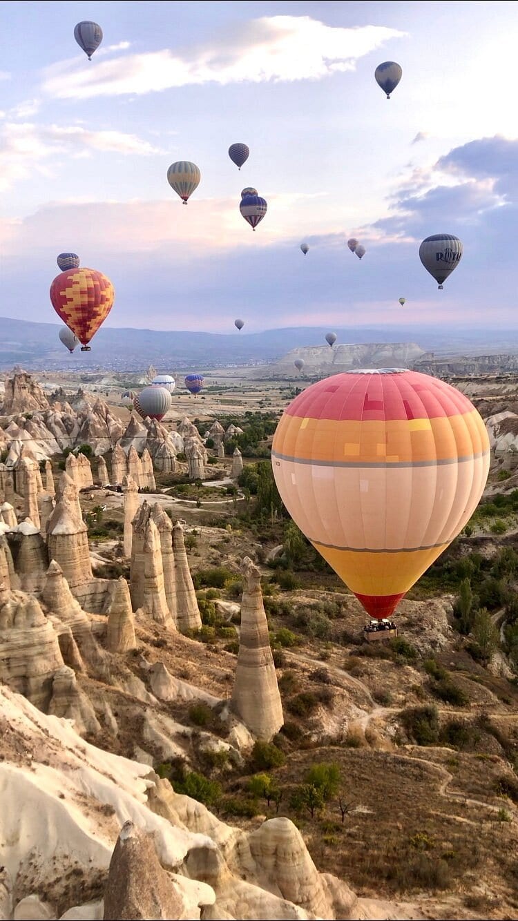 Una mongolfiera rosa e arancione che scivola bassa sugli alti camini delle fate della Valle dell’Amore in Cappadocia all’alba