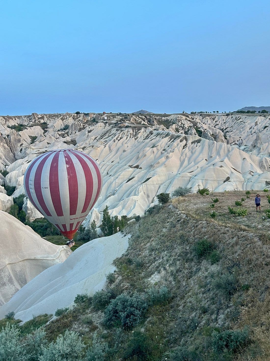 Una sola mongolfiera a righe rosse e bianche che vola bassa sulle creste chiare della Valle Bianca in Cappadocia al crepuscolo