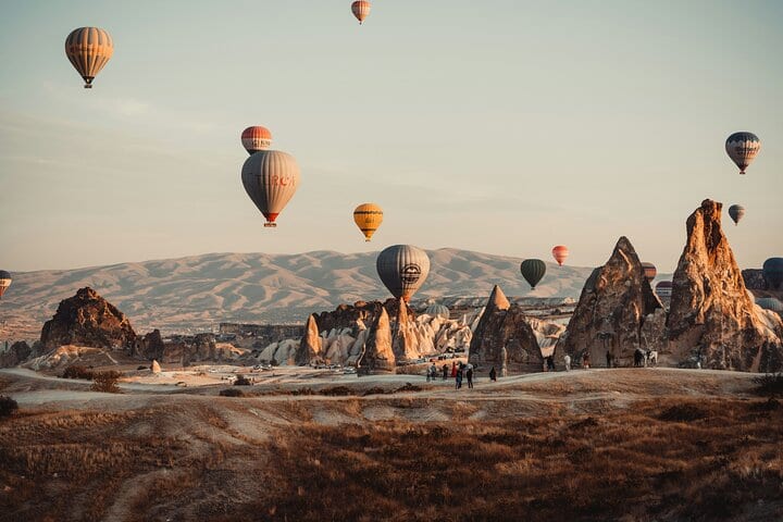Mongolfiere che scivolano sui camini delle fate di Göreme nella luce dorata del mattino, con persone che camminano in basso