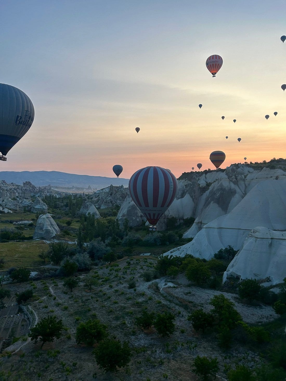 Mongolfiere che scivolano sulle valli della Cappadocia sotto un cielo dell’alba arancione intenso
