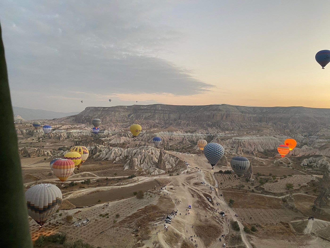 Mongolfiere che decollano attraverso la valle della Cappadocia all’alba, viste da una mongolfiera già in volo