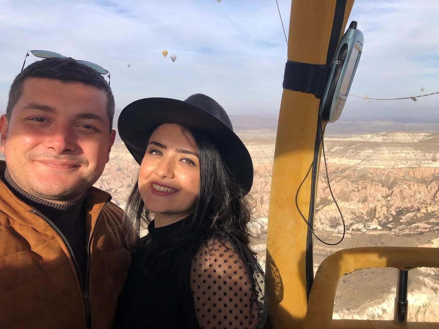 Una giovane coppia che si fa un selfie nella cesta di una mongolfiera sulla valle della Cappadocia all’alba, con uno strumento di volo accanto