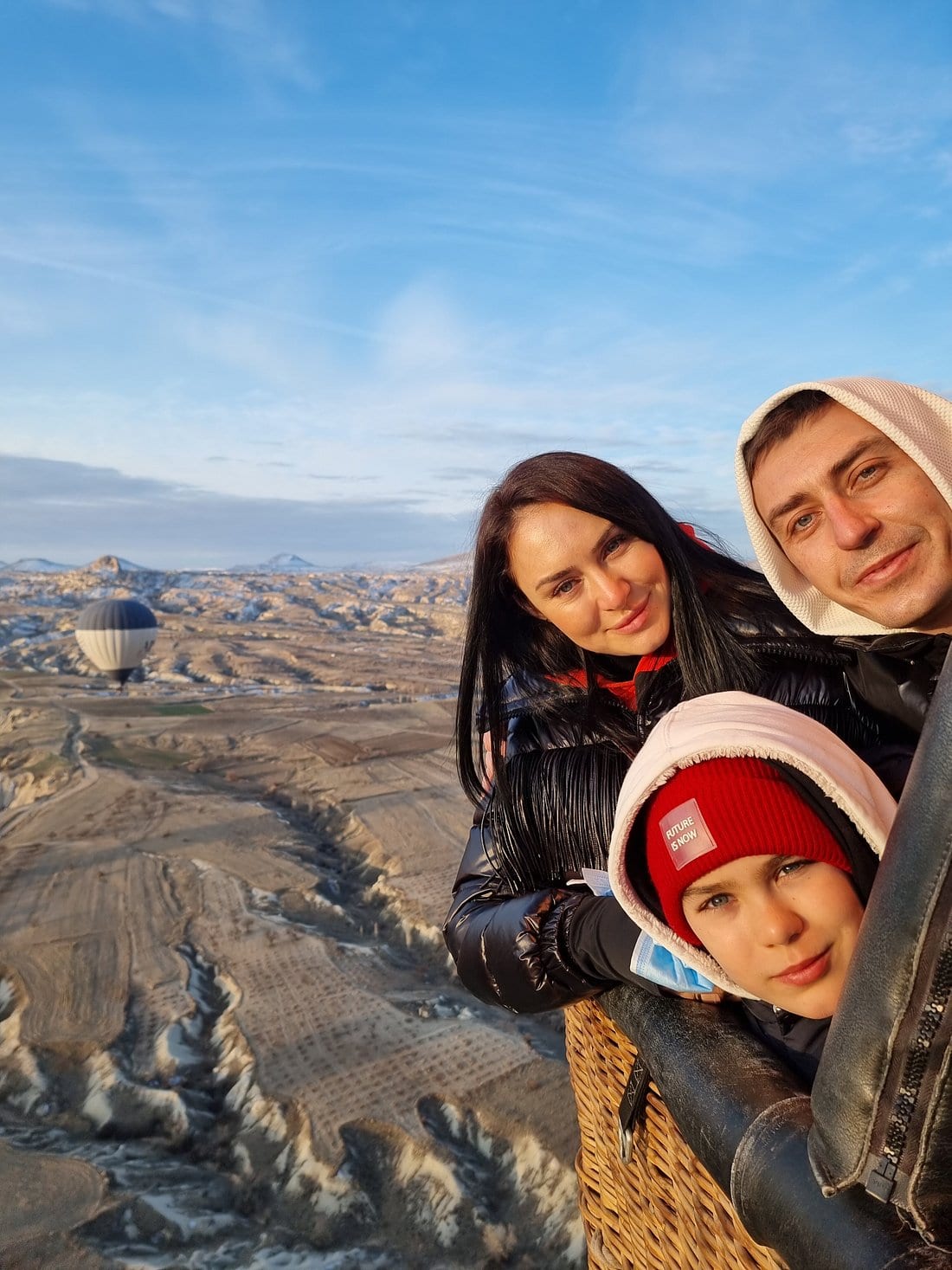 Una mamma, un papà e il figlio che si fanno un selfie nella cesta di una mongolfiera sulle valli della Cappadocia all’alba