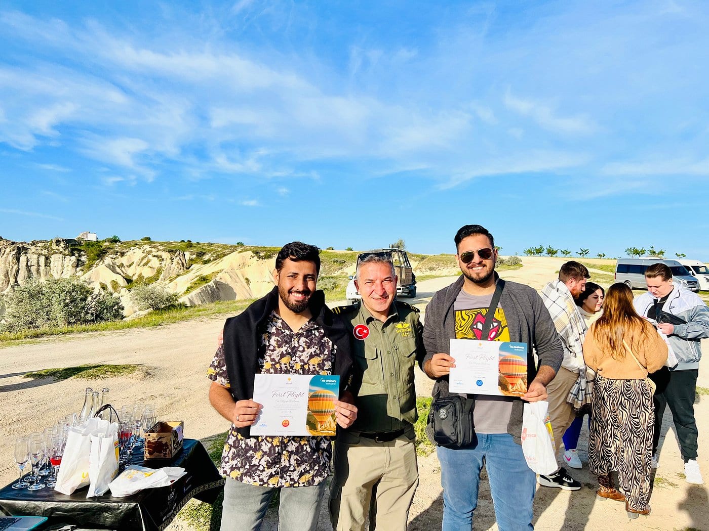 Due ospiti che tengono i loro certificati di volo personalizzati accanto al pilota al punto di atterraggio in Cappadocia