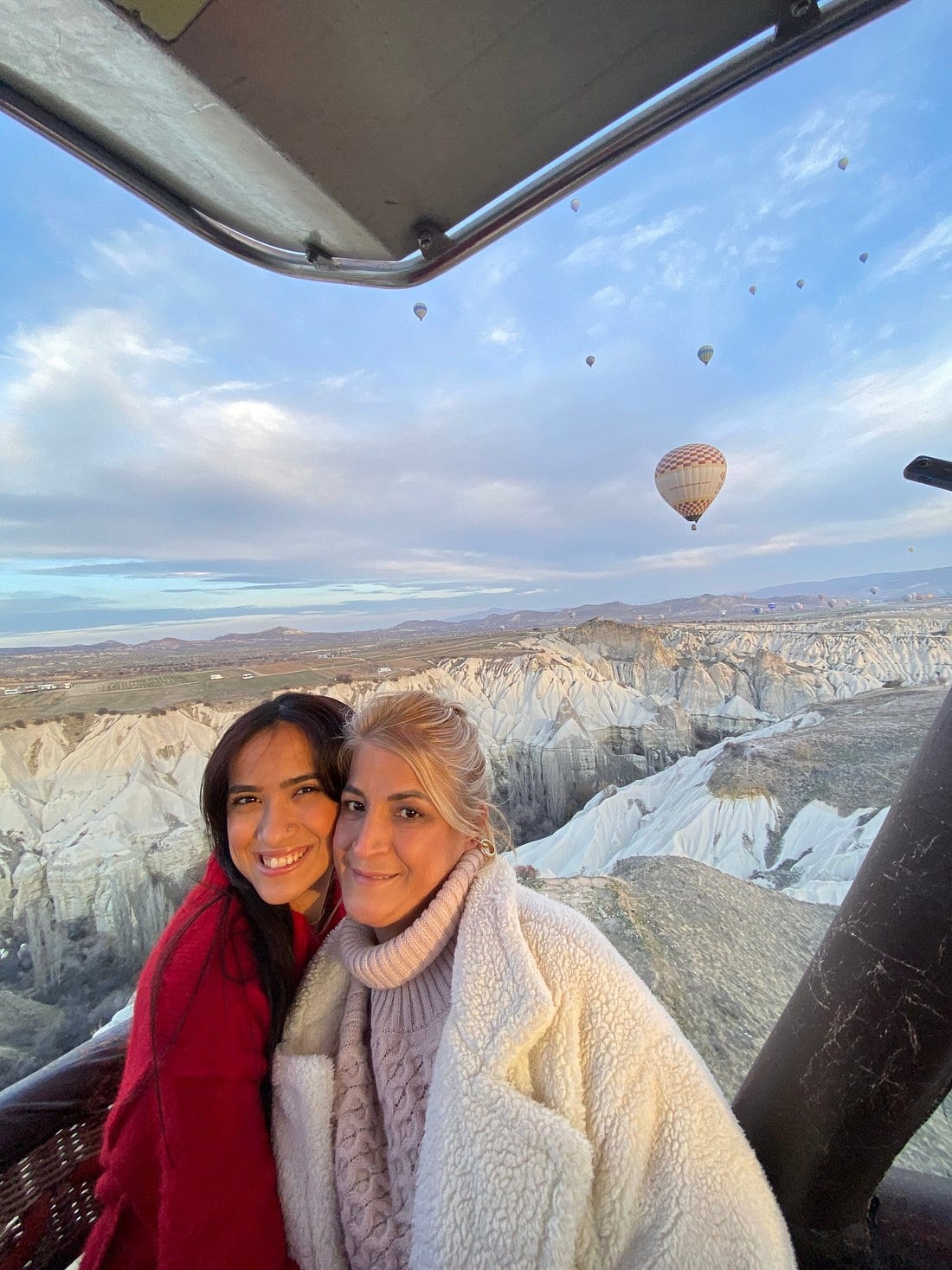 Due ospiti che sorridono insieme nella cesta di una mongolfiera sopra le creste bianche della Valle Rossa in Cappadocia