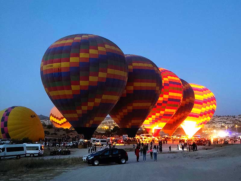 A hot air balloon lifting off at sunrise over the Cappadocia valleys