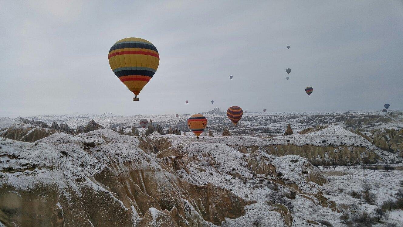 Hot air balloons drifting over a snow-dusted Cappadocia valley on a clear winter morning