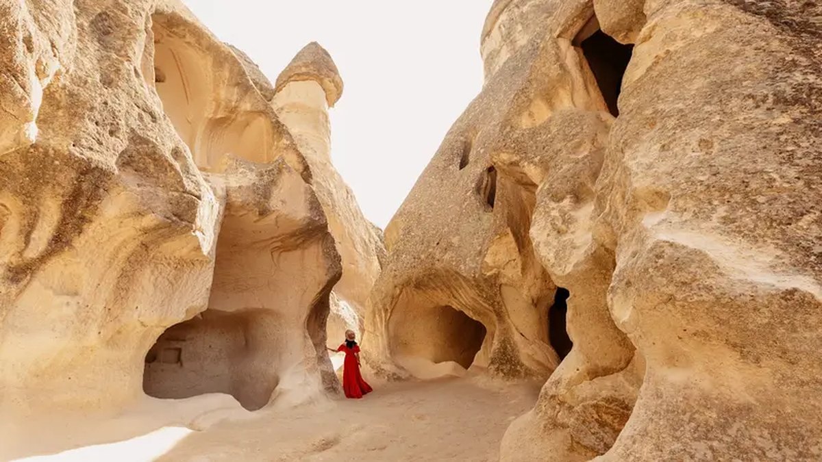 A solo traveler in a red dress walking calmly between the fairy chimneys of Pasabag Valley in Cappadocia