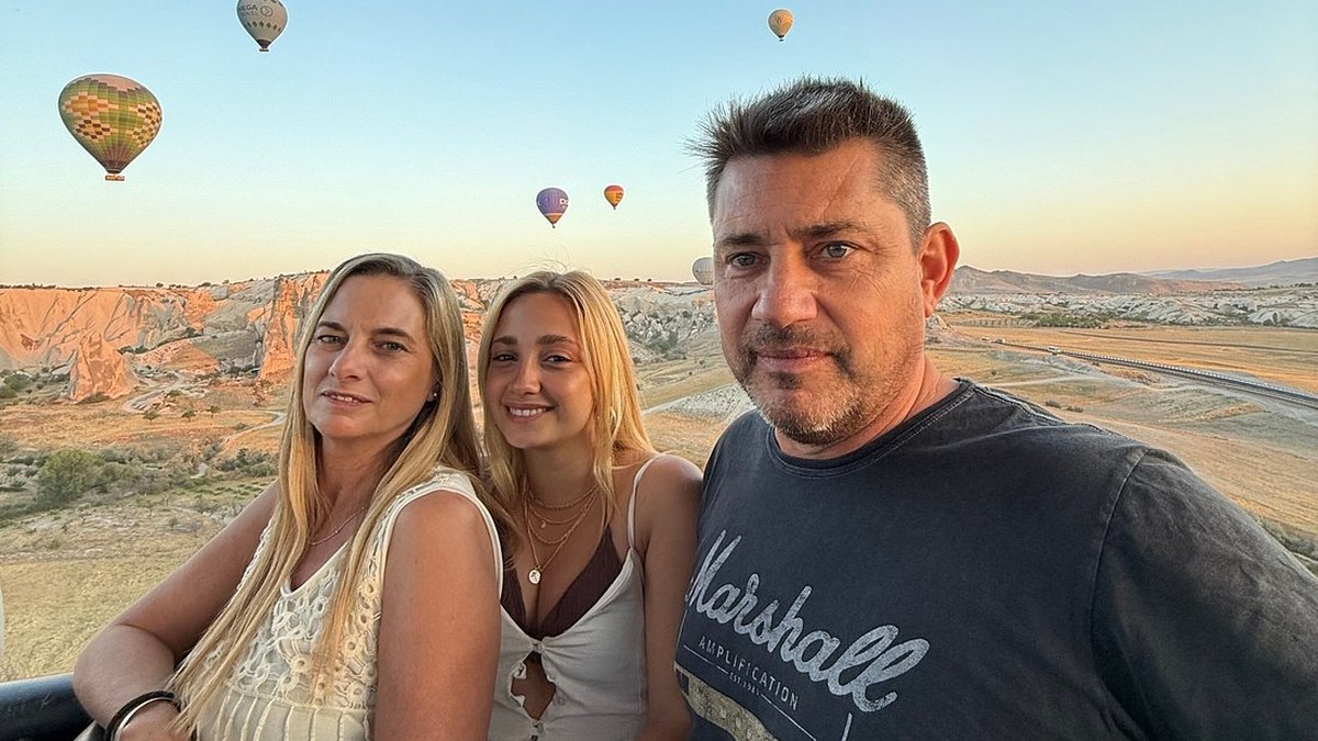 A guest on a terrace at sunrise in Göreme, with dozens of hot air balloons rising over the Cappadocia valleys behind her