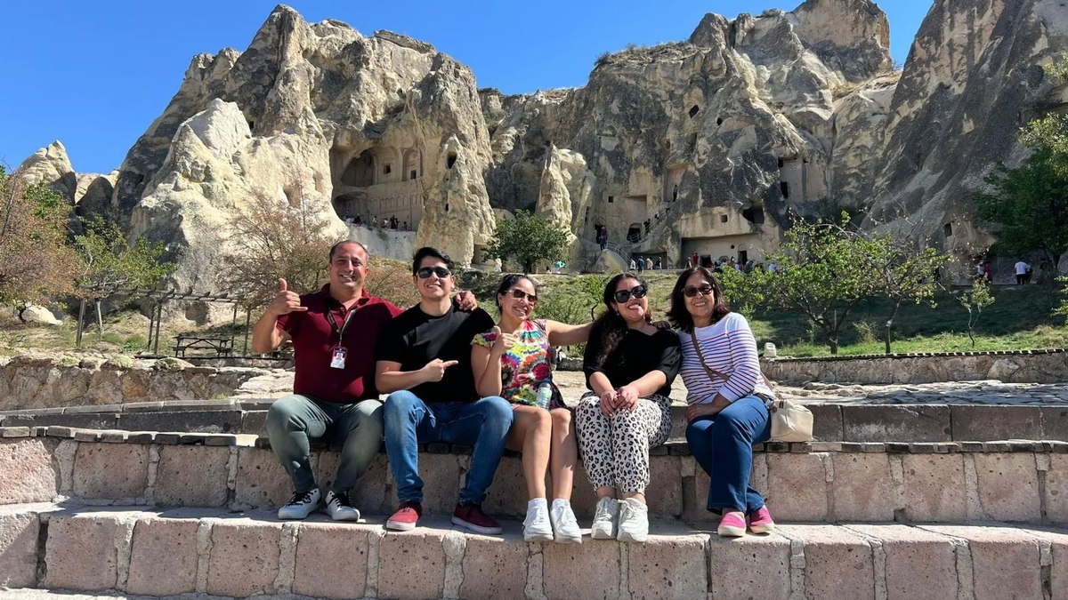 Five guests with their professional licensed guide seated at the entrance of Göreme Open-Air Museum, with the rock-cut cave churches and chapels of the UNESCO World Heritage site rising in the background