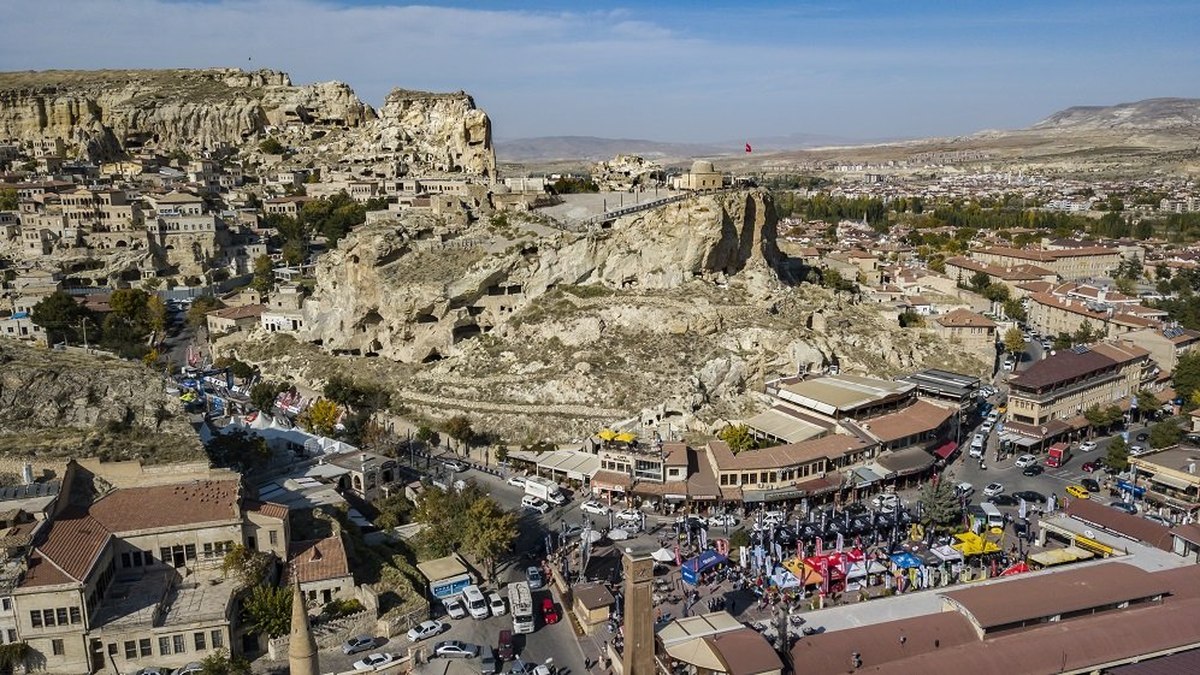 Aerial panorama of Ürgüp showing the working Turkish town, its central rock outcrop with the Temenni hill and Turkish flag, and the surrounding cave landscape