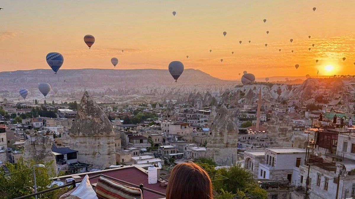 A guest watching dozens of hot air balloons rise above Goreme at sunrise from a Cappadocia rooftop terrace, the iconic morning view that defines what time hot air balloons fly in the region